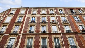 Un immeuble à plusieurs étages, caractérisé par un style architectural uniforme, avec des fenêtres régulièrement espacées, des balcons dotés de garde-corps en métal et un toit plat.