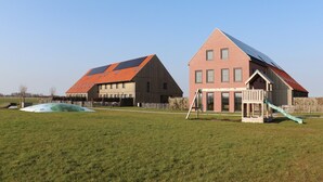 Un barrio residencial con dos casas, una con techo rojo y paneles solares, y otra con fachada de ladrillo y una pequeña casita de madera con un tobogán.