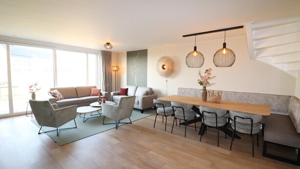 Una sala de estar moderna con un sofá, sillones, una mesa de comedor con sillas, una mesa de centro y lámparas colgantes.