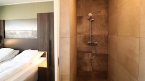 A modern bathroom with a shower, a bed with white linens, and a view of a landscape through the window. - Luxury waterfront villa (leons)