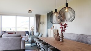 A modern living room with a sofa, dining table, and chairs, large windows, and decorative lighting. - Luxury waterfront villa (leons)
