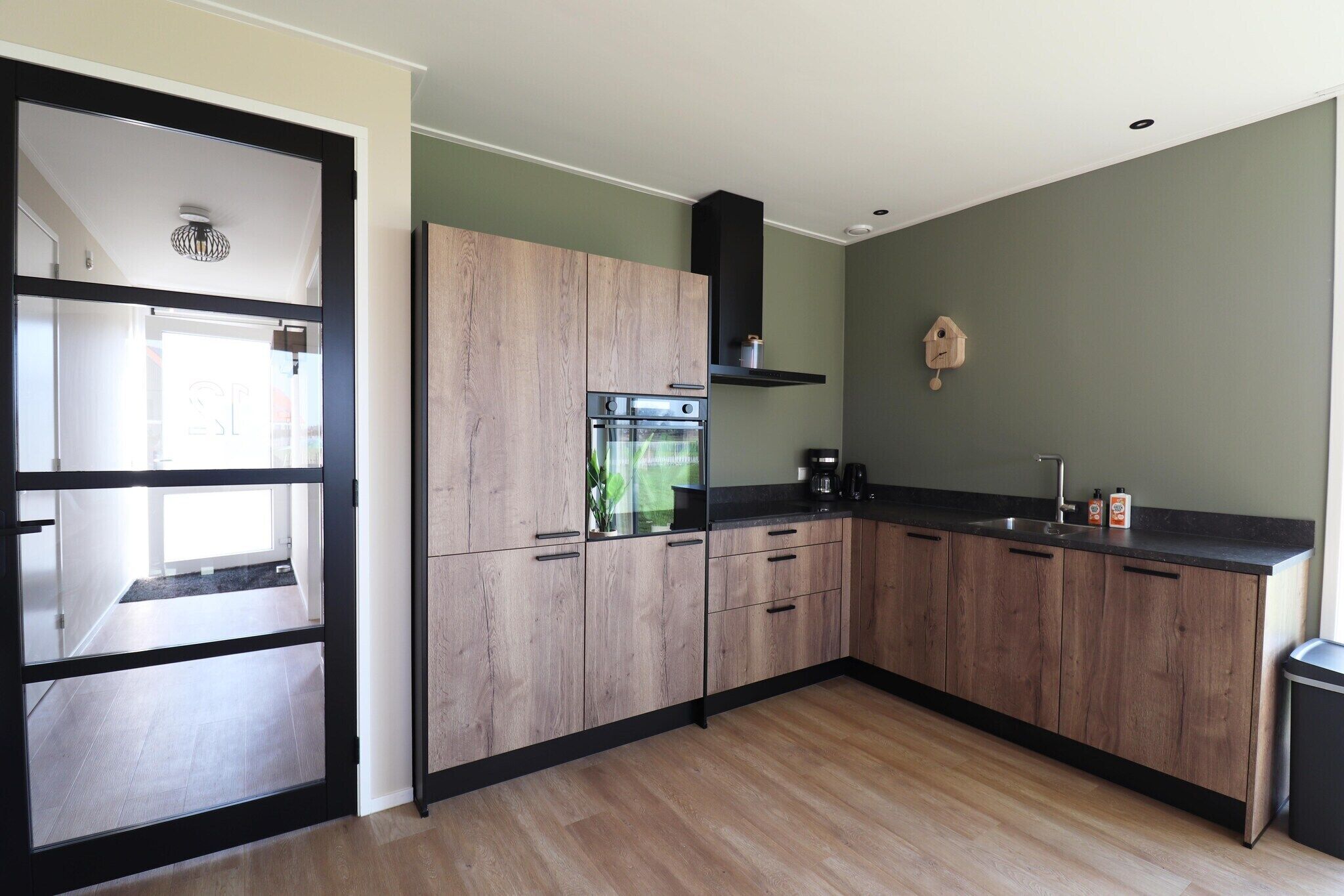 Une cuisine moderne avec des meubles en bois, un four encastré et un plan de travail noir.