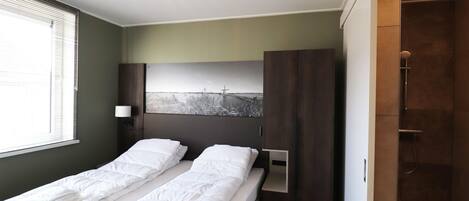 A bedroom with a bed, a nightstand, a wall-mounted lamp, a painting, and a shower area.