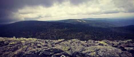 A rocky landscape with a person's feet on a rock, overlooking a forested valley under a cloudy sky.