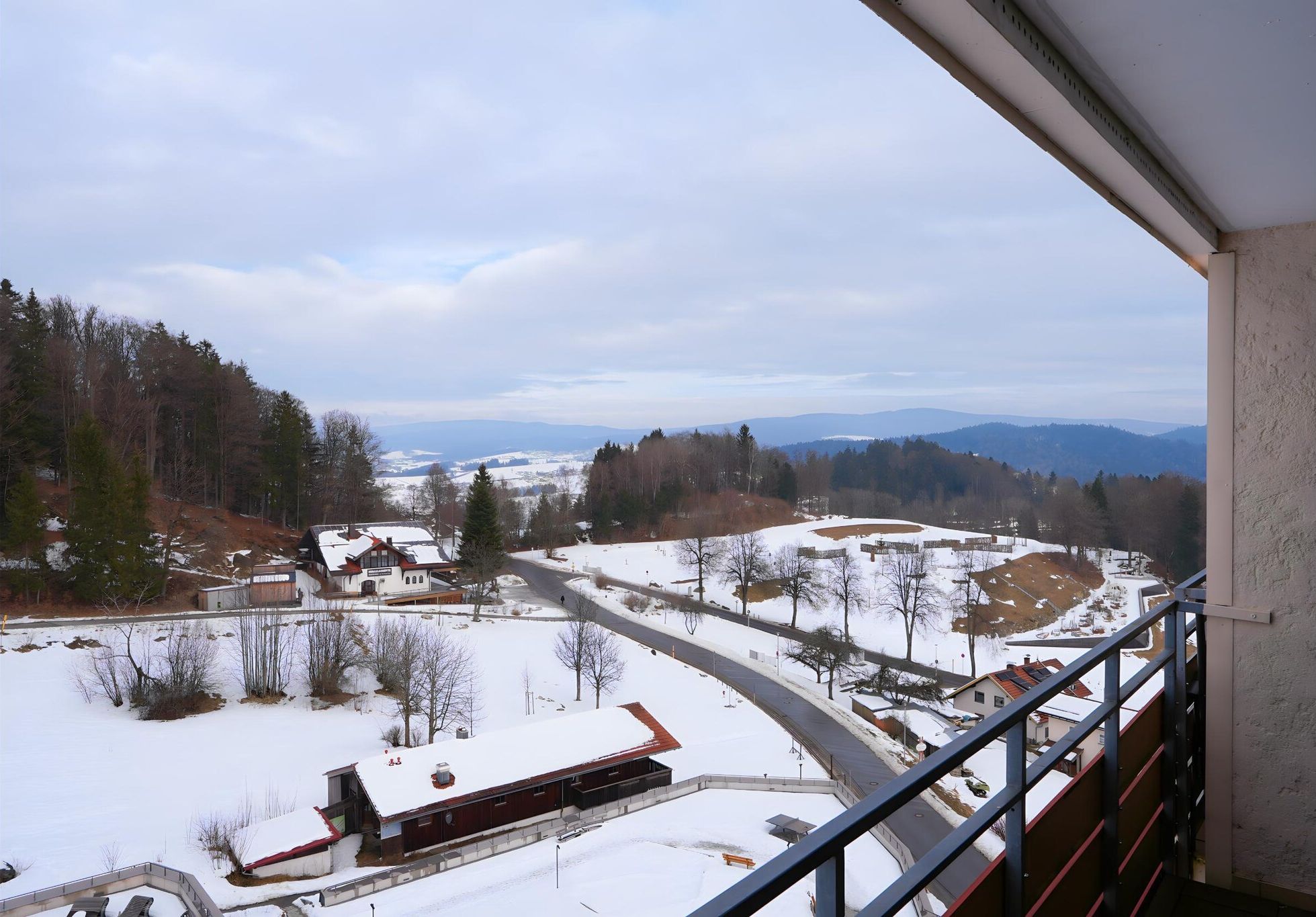 A snowy landscape with a road, buildings, and trees.
