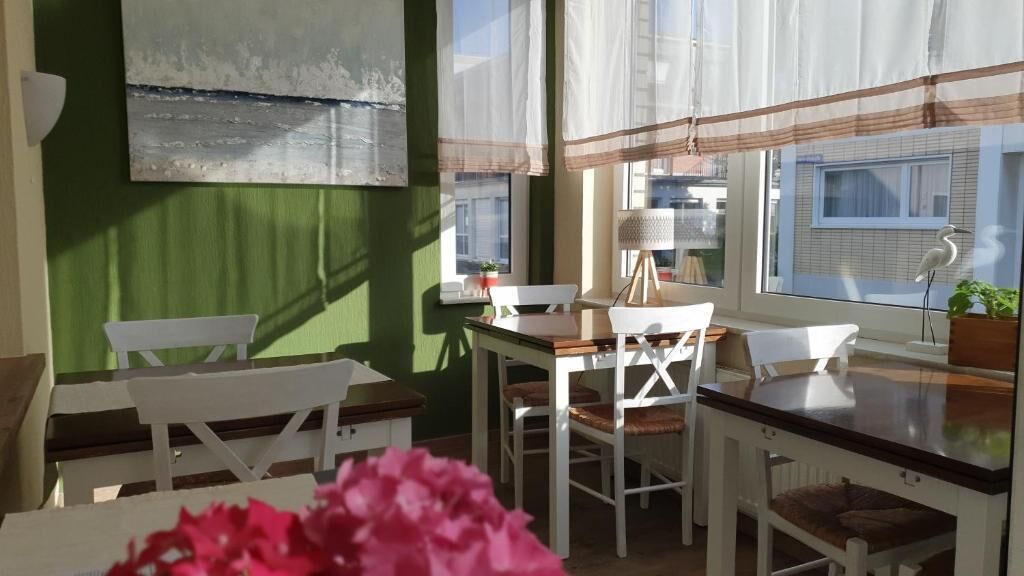 A dining area with a table and chairs, a window with curtains, and a painting on the wall.