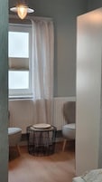 A small room with a window, a radiator, a round table with a plate, and a chair.