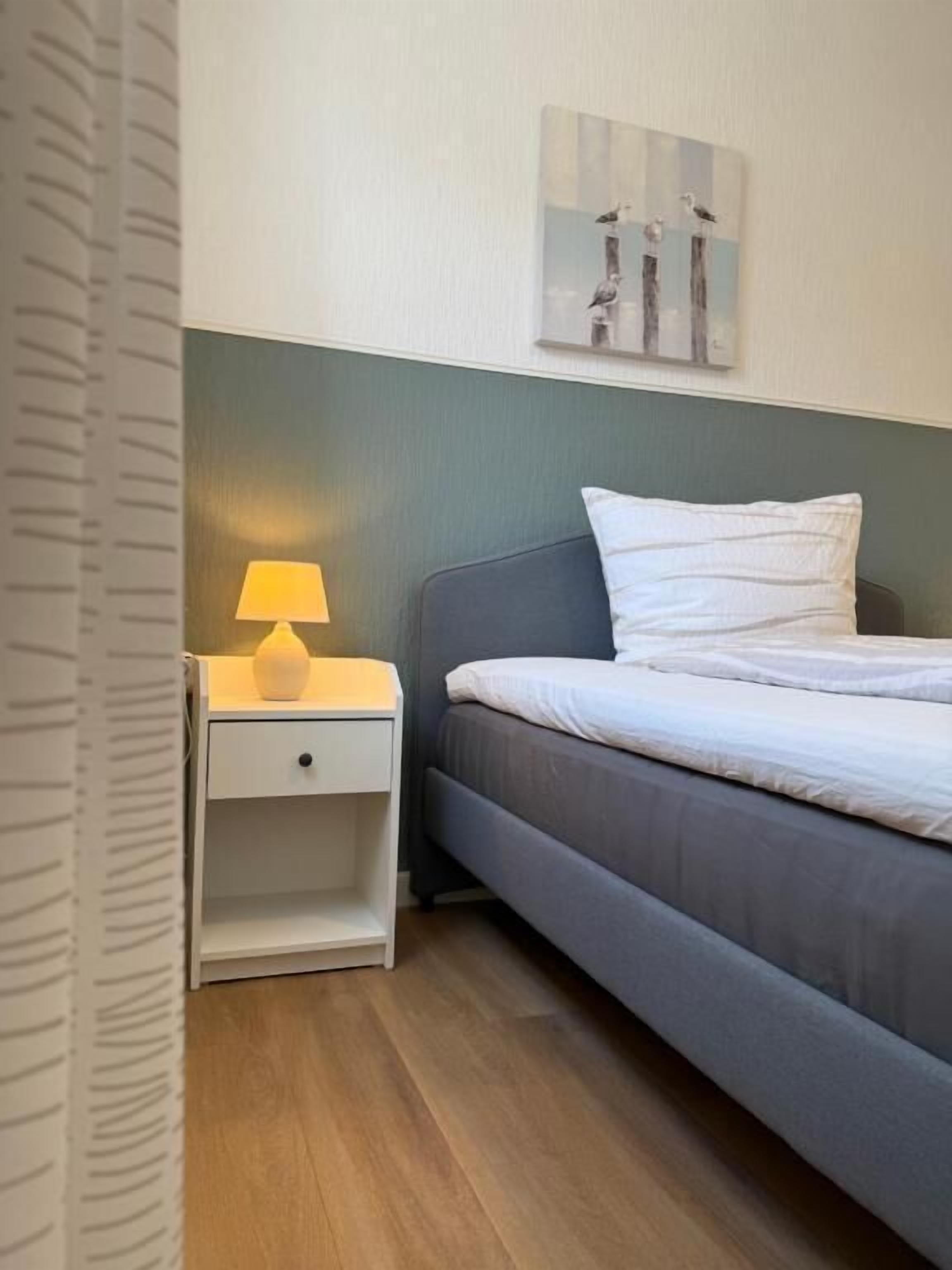 A bedroom with a bed, a nightstand with a lamp, and a wall-mounted artwork.