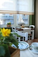 A dining area with a table set for two, a window with a view of buildings, and a small sailboat model on the windowsill.
