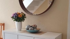 A white cabinet with wicker baskets, a vase with flowers, and a mirror reflecting a staircase. - Seemoi (Norderney)