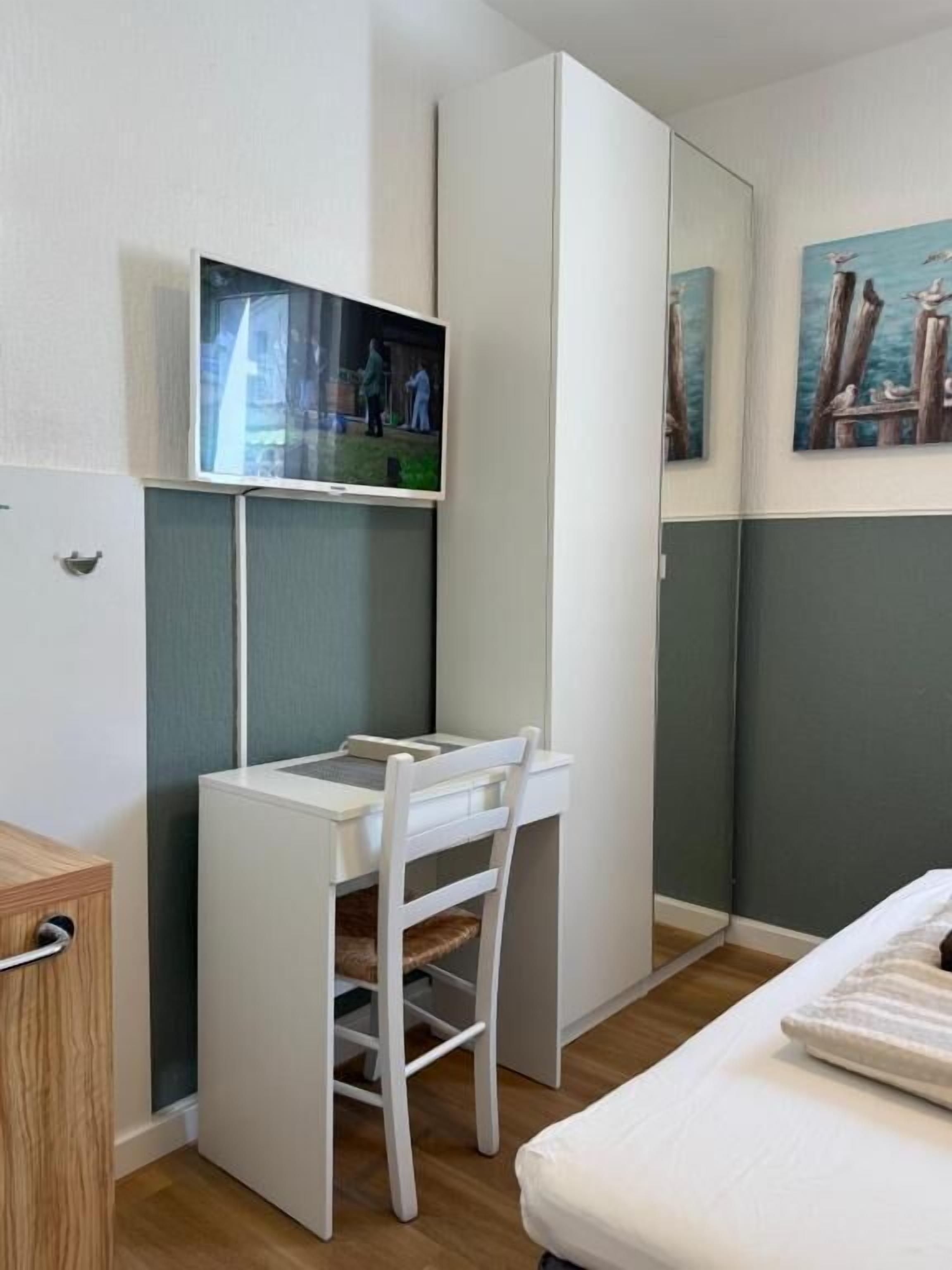 A compact room with a bed, a desk with a chair, a television, and a painting on the wall.