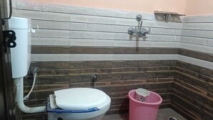 Un baño con inodoro, un cubo de basura rosa y una ducha.