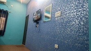 Una habitación con pared azul con textura, un televisor montado en la pared, una ventana con espejo y una puerta.