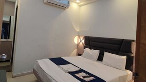 Une chambre d’hôtel moderne équipée d’un lit, d’un ventilateur de plafond, d’un climatiseur et d’un luminaire fixé au mur.