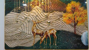 Une œuvre d’art murale représentant des cerfs et un arbre, avec un luminaire placé au-dessus.