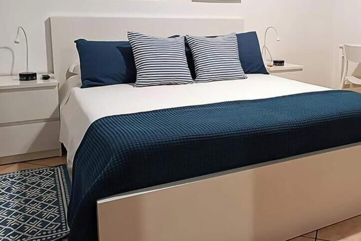 A bed with a white headboard, two bedside tables, and three framed artworks on the wall.
