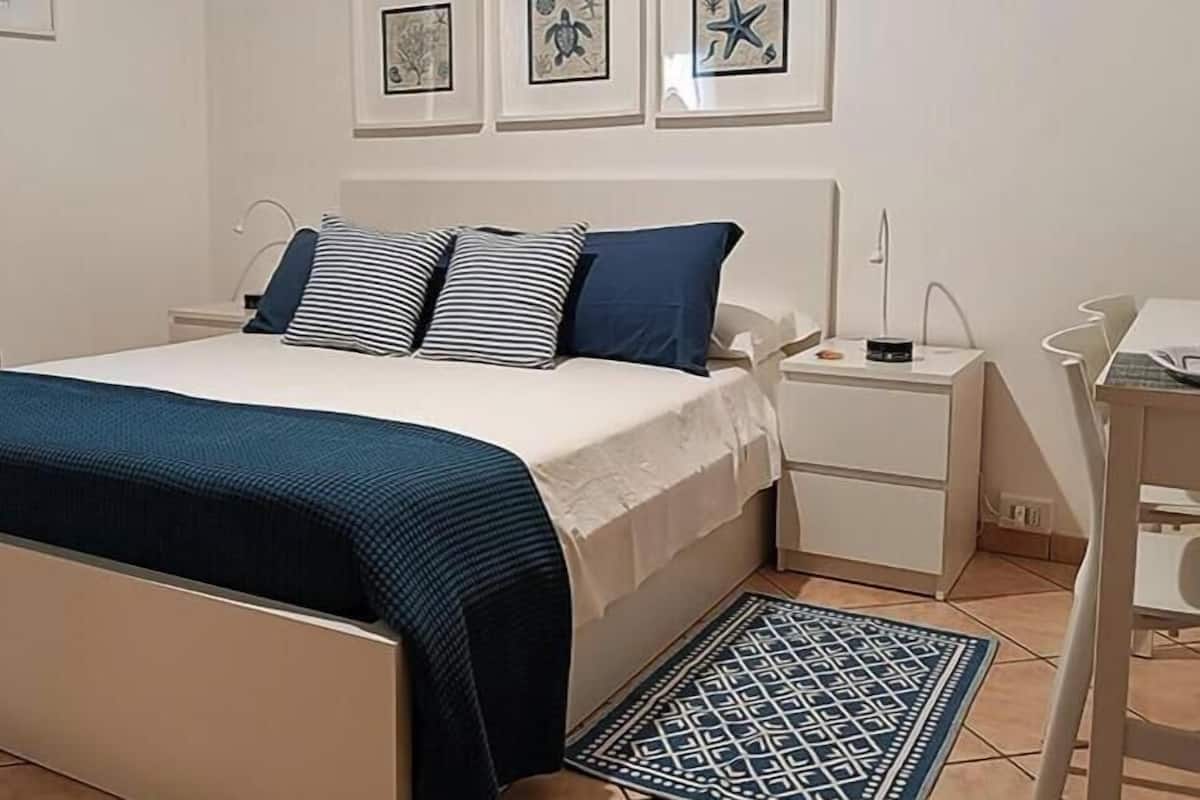 A neatly arranged bedroom with a bed, bedside tables, a desk, and a patterned rug.
