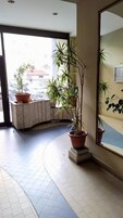 Una hall d'albergo con piante in vaso, un grande specchio e un pavimento a mosaico curvo.