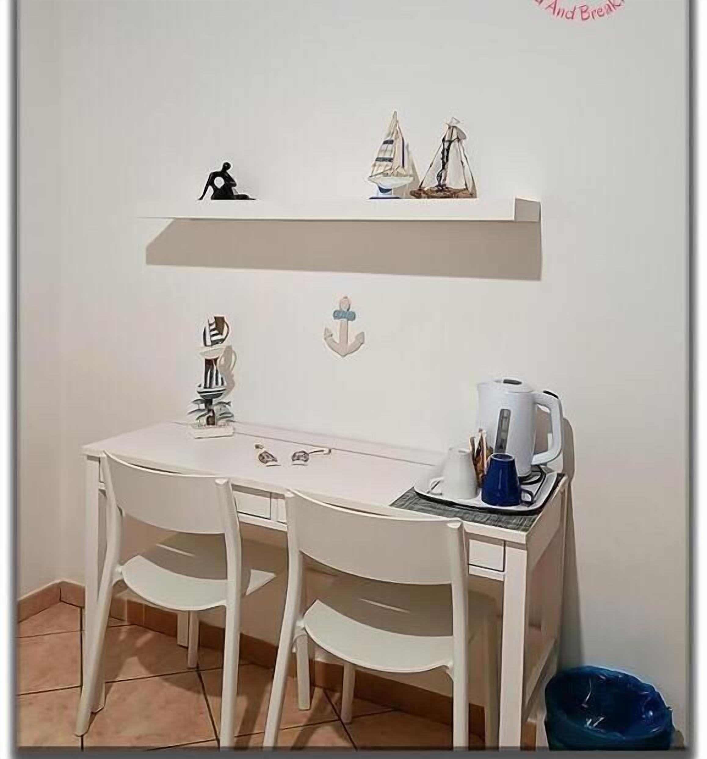 Un petit bureau blanc avec deux chaises, une étagère au-dessus où sont posés une figurine et un petit modèle de voilier, ainsi qu’une décoration en forme d’ancre fixée au mur.