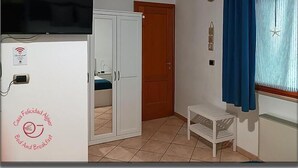 Una habitación con cama, armario, televisor, una mesita y ventana con cortinas.