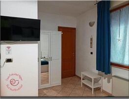 Una stanza con un letto, un armadio, una televisione, un tavolino e una finestra con tende.