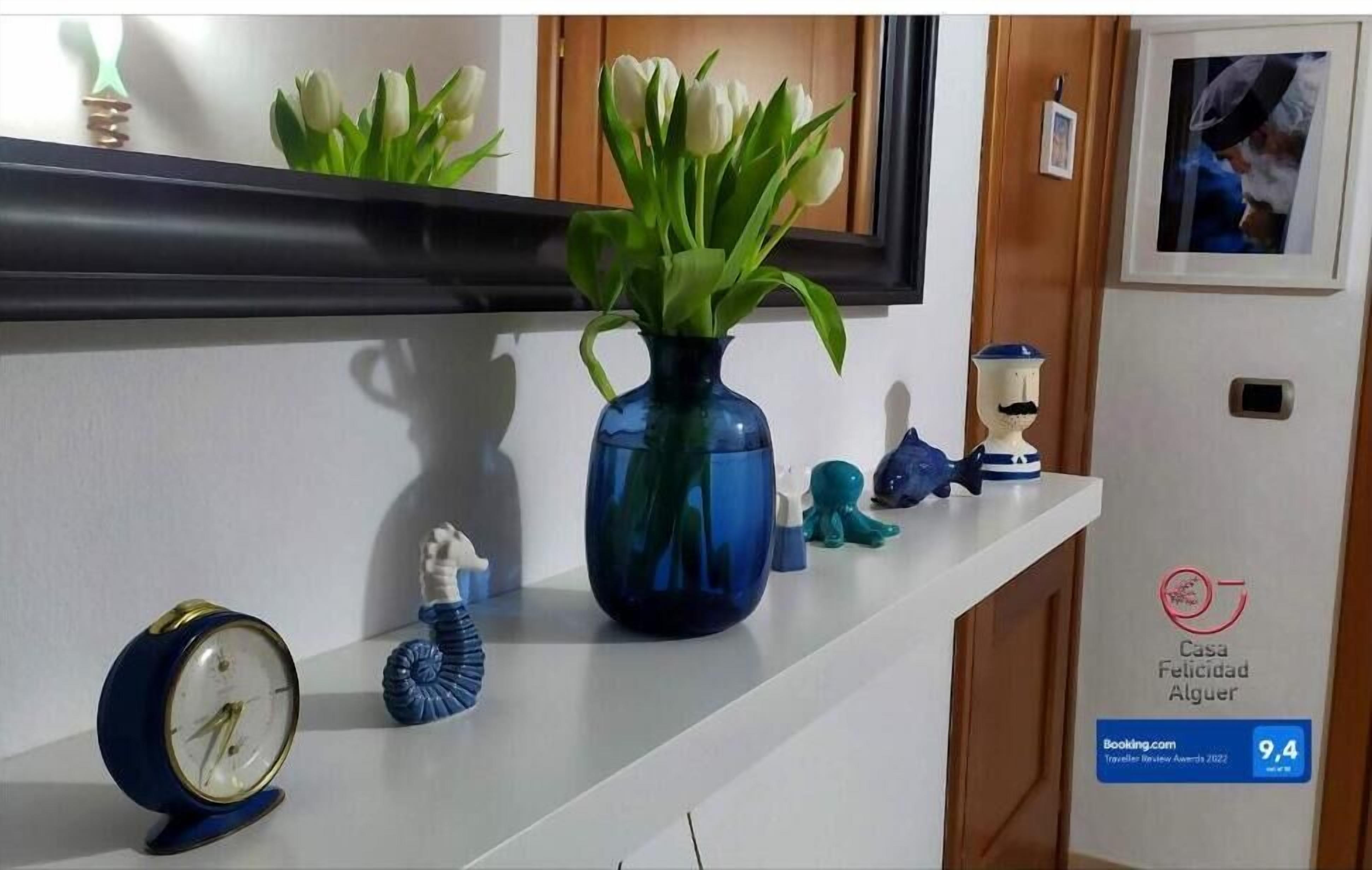 Un espace d’accueil d’hôtel avec un vase bleu rempli de fleurs, une horloge et un certificat encadré accroché au mur.