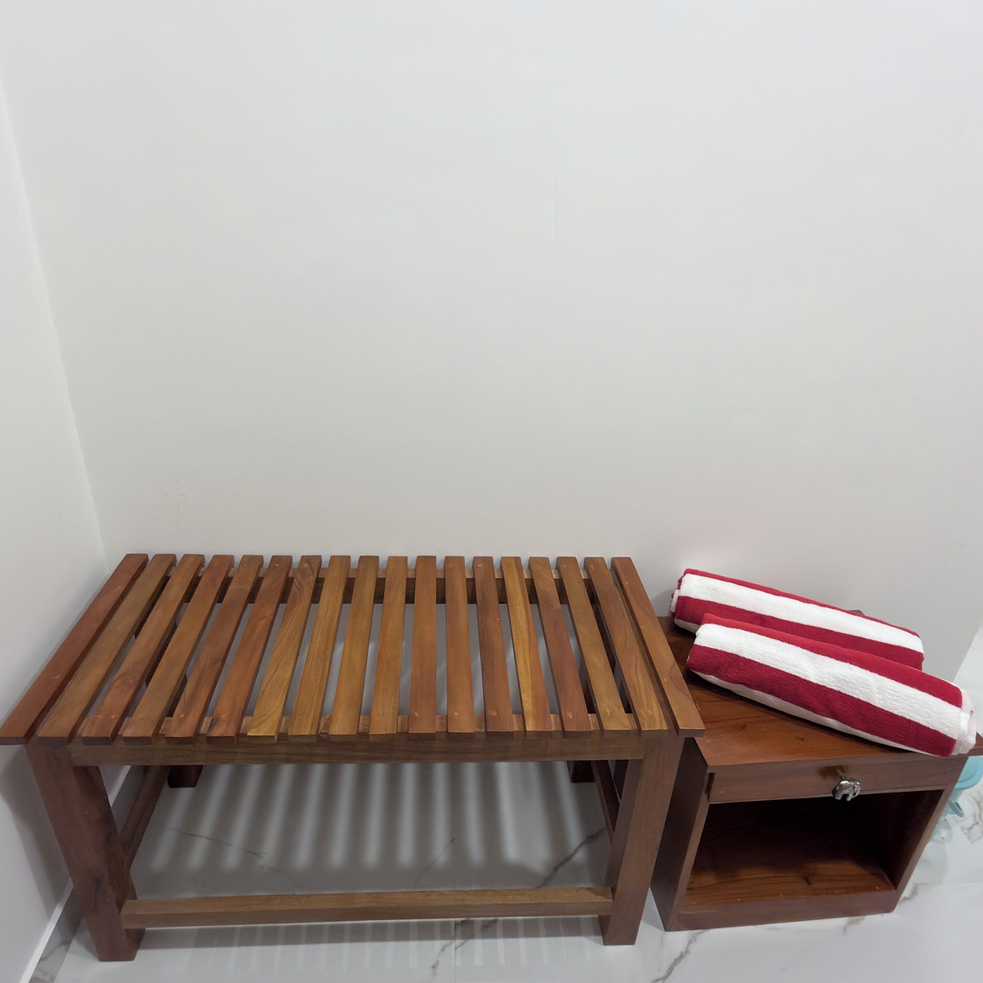 Un banc en bois avec une étagère inférieure, une petite boîte en bois dotée d’un tiroir, et une serviette rouge et blanche.