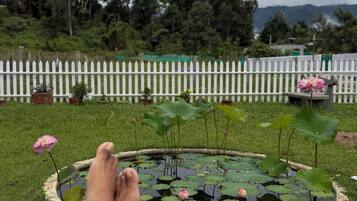 A person's feet resting on a stone ledge overlooking a pond with lotus flowers and a white picket fence in the background.