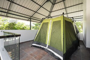 A green tent with a white stripe, set up on a tiled floor under a metal roof.