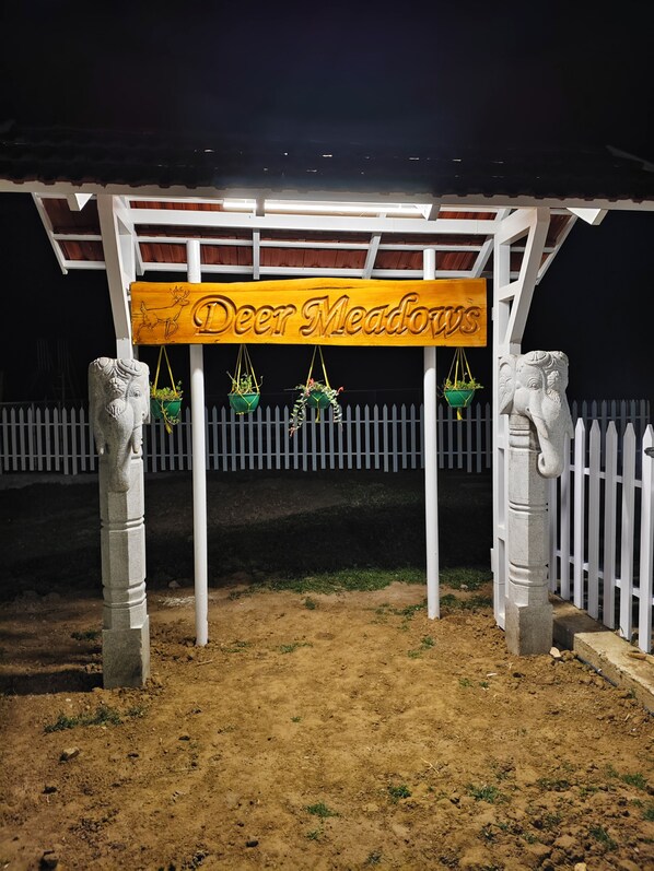 A wooden sign with the text 'Deer Meadows' hanging under a white structure with stone pillars. - Deer Meadows (Mudumalai)