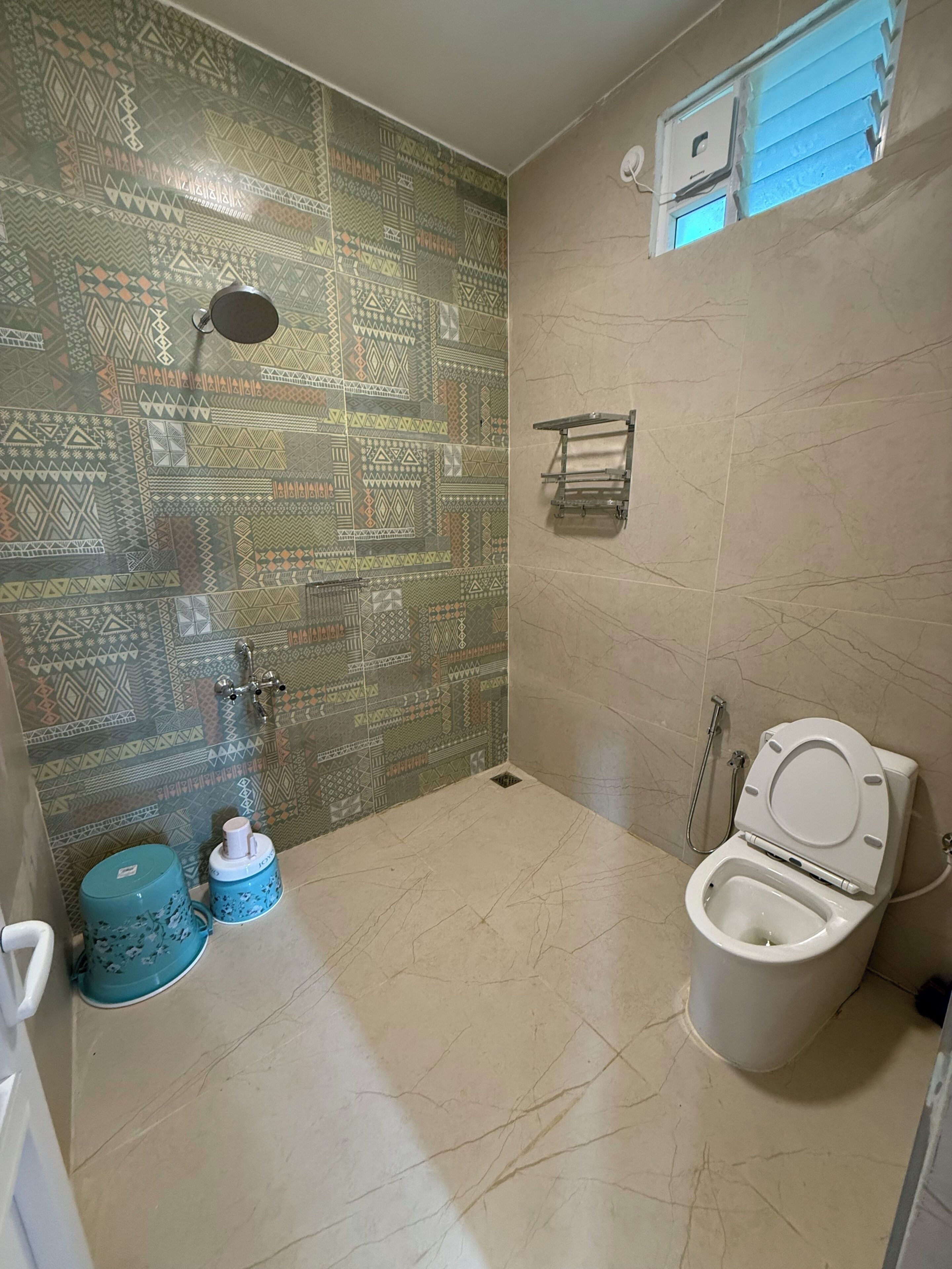 Un baño con pared decorada, inodoro, ducha y una ventana pequeña.