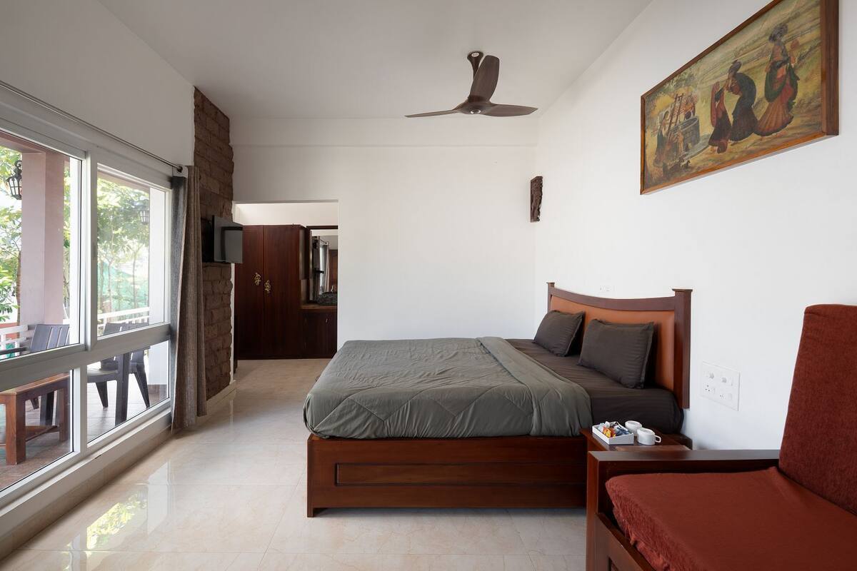 A bedroom with a bed, a ceiling fan, a painting, and a view through a window.