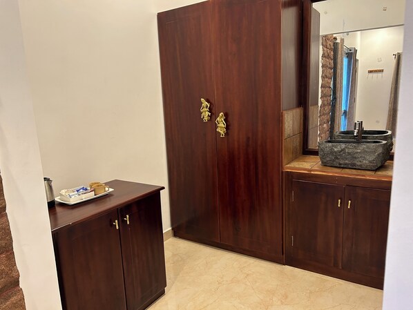 A wooden wardrobe with brass handles, a small table with a tray, and a stone sink. - Deer Meadows  (Mudumalai)