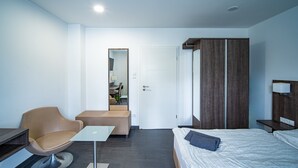 A modern hotel room with a bed, a chair, a small table, a wardrobe, and a door leading to a bathroom. - Spacious, Comfortable Apartments in a Quiet Setting Near Cologne (Pulheim)