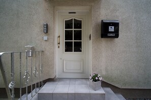Una puerta blanca con cerradura electrónica, un buzón pequeño y una maceta en los escalones.