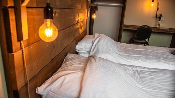 A room with a wooden headboard, two beds with white bedding, and hanging light fixtures. - Bij de 3 linden (Wijchen)