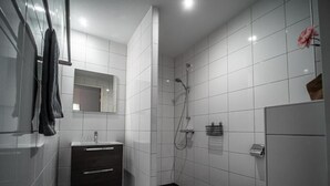 A modern bathroom with white tiles, a shower, a toilet, and a mirror. - Bij de 3 linden (Wijchen)