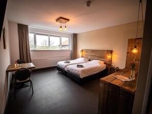 A hotel room with two beds, a desk, a chair, a wooden headboard, and a window with curtains. - Bij de 3 linden (Wijchen)