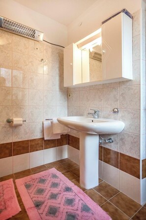 Ein Badezimmer mit einem weißen Waschbecken, einem Handtuchhalter, einem Spiegel und einer rosa Fußmatte.
