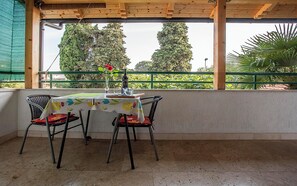 Ein überdachter Außenbereich mit Tisch und Stühlen, Blick auf Bäume und einer Brüstung.
