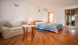 Ein Schlafzimmer mit Bett, Holzboden, Holztür, einem kleinen Tisch mit Stuhl und einer Couch.