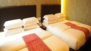 Een hotelkamer met twee bedden, elk voorzien van witte lakens en een rode sierkussen.