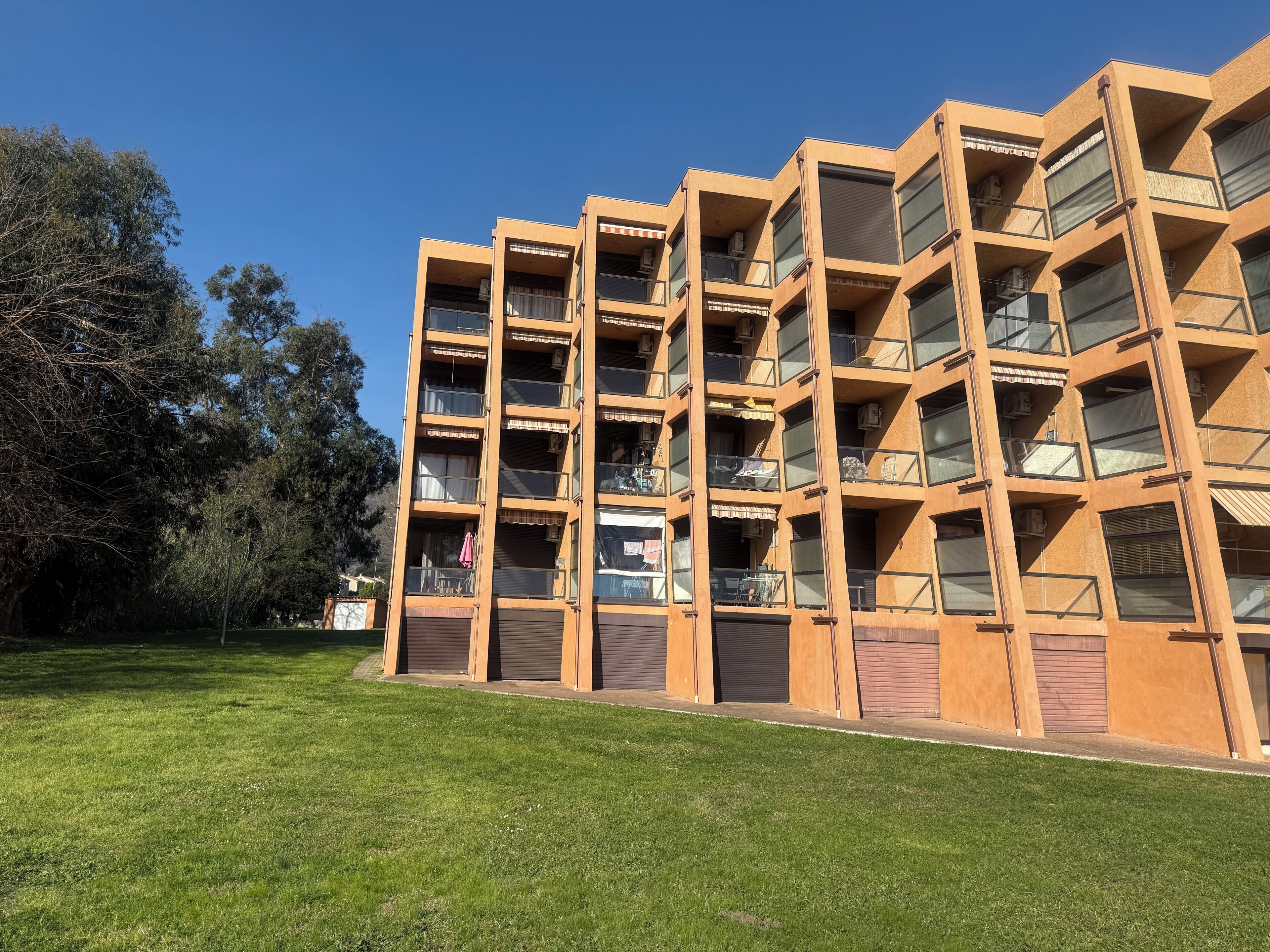 Un immeuble à plusieurs étages doté de balcons, de grandes fenêtres et d’un espace verdoyant à l’avant.