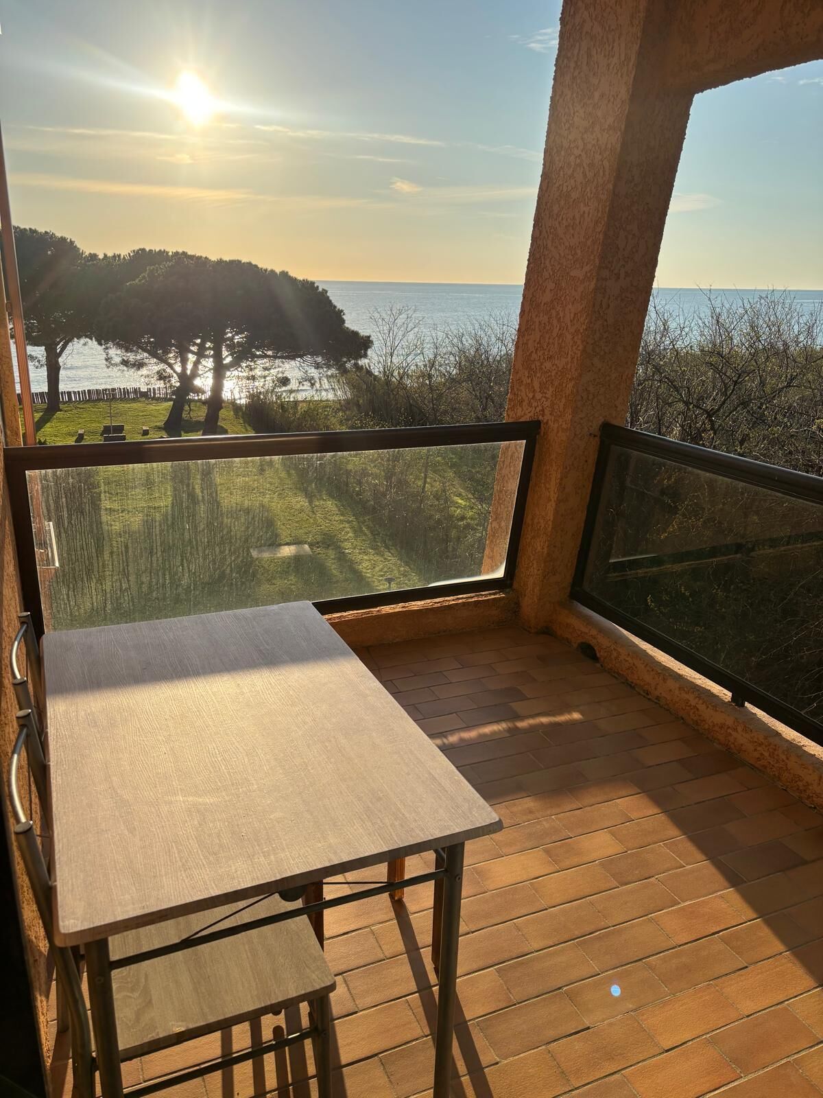 Ein Balkon mit Tisch und Stühlen, der auf ein Gewässer und Bäume blickt.