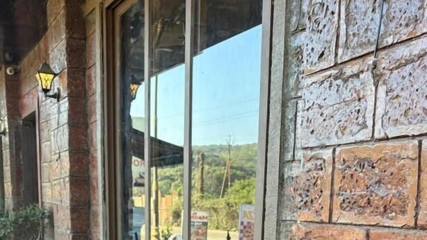 A building with a stone facade, a window with a view of the landscape, and a flower bed with various flowers. - Art of Greens Hotel (Mahabaleshwar)