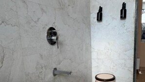 A bathroom with a marble wall, a toilet, a bidet, and a trash bin. - Art of Greens Hotel (Mahabaleshwar)