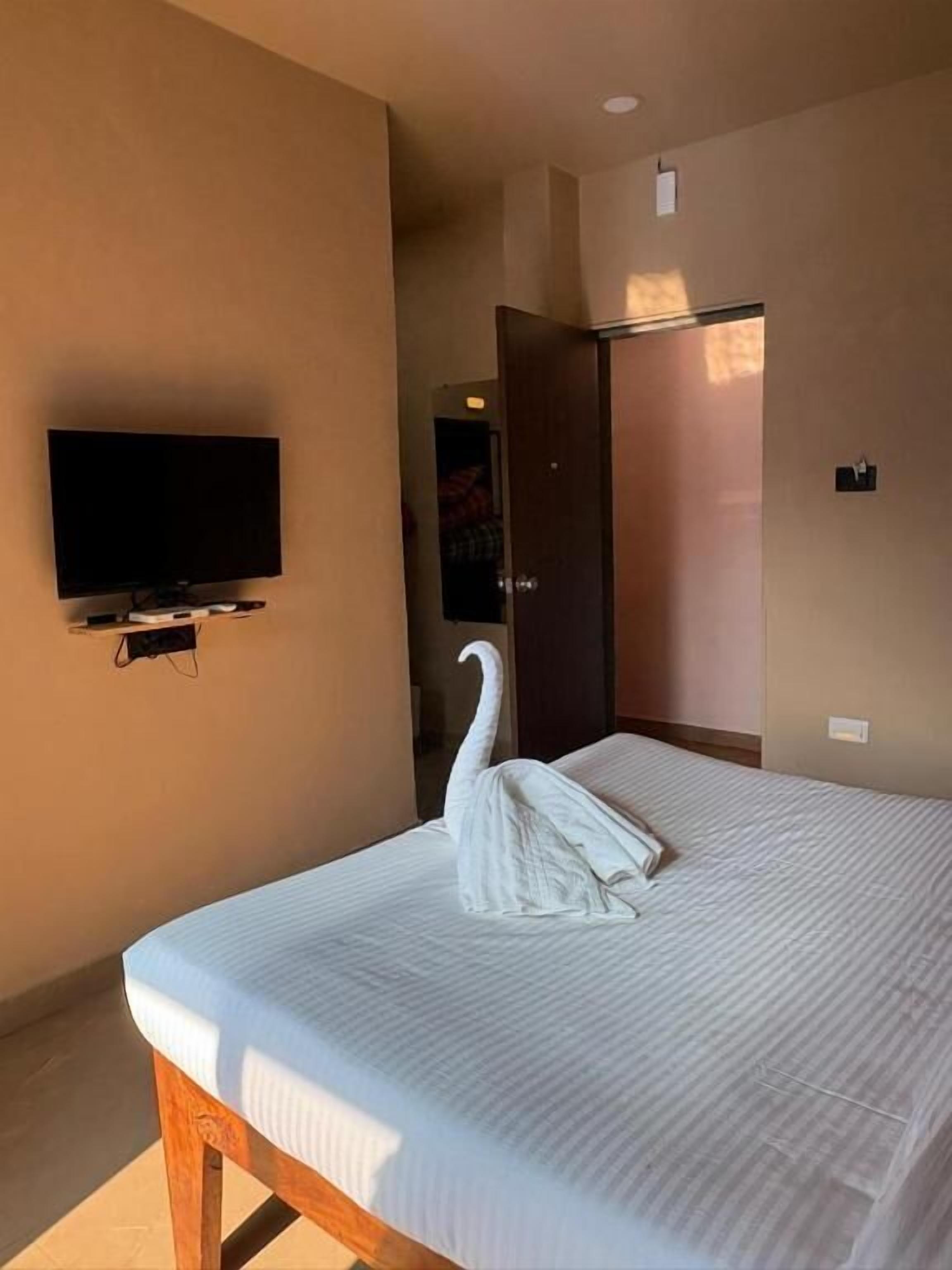 A hotel room with a bed, a flat-screen TV mounted on the wall, and a door leading to another room.