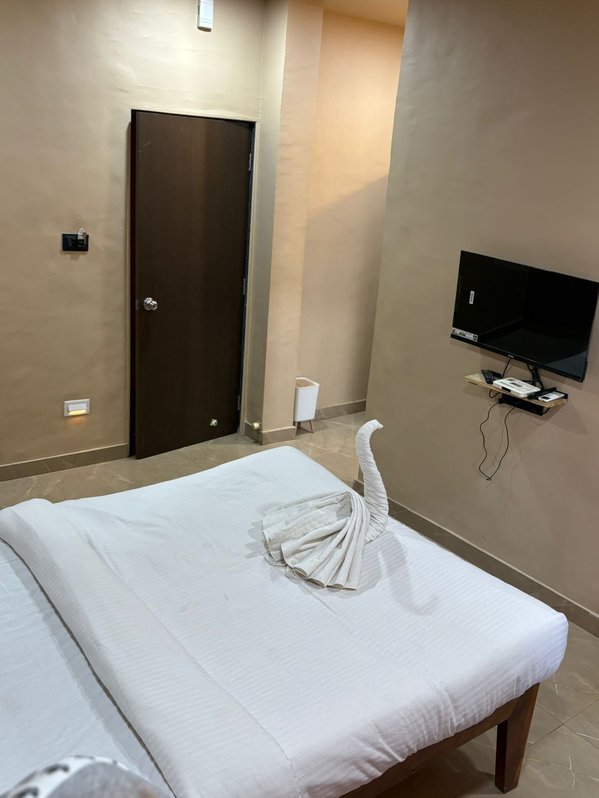 Une chambre d’hôtel avec un lit, une télévision, une porte et un interrupteur.