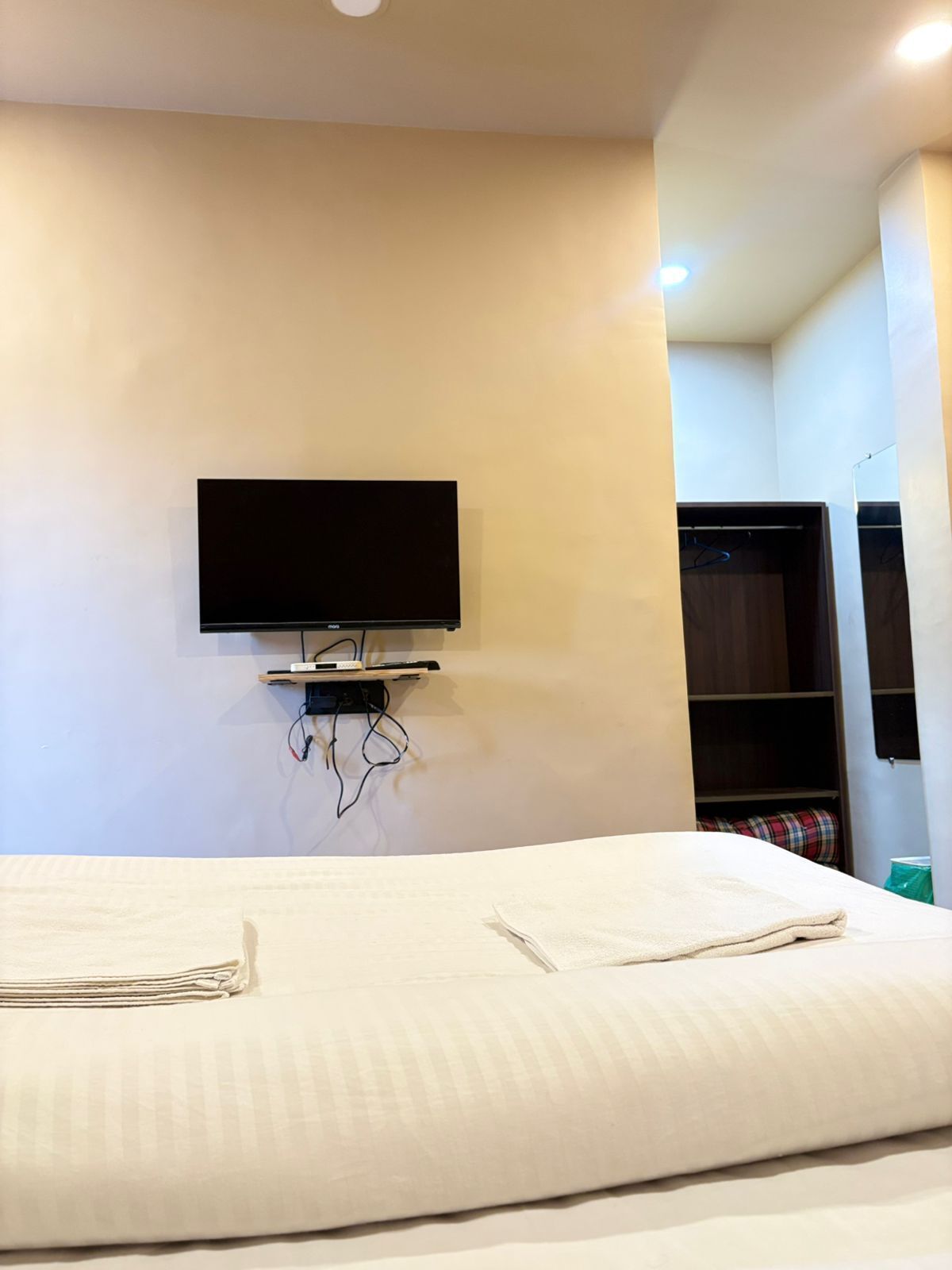 Een hotelkamer met een bed, een flatscreen televisie aan de wand en een kast met hangende kleding.