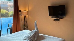 A hotel room with a bed, a TV mounted on the wall, and a balcony with a view. - Art of Greens Hotel (Mahabaleshwar)